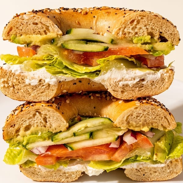 Two stacked Ben & Esther's everything bagels with cream cheese, avocado, lettuce, tomato, cucumber, and onion.