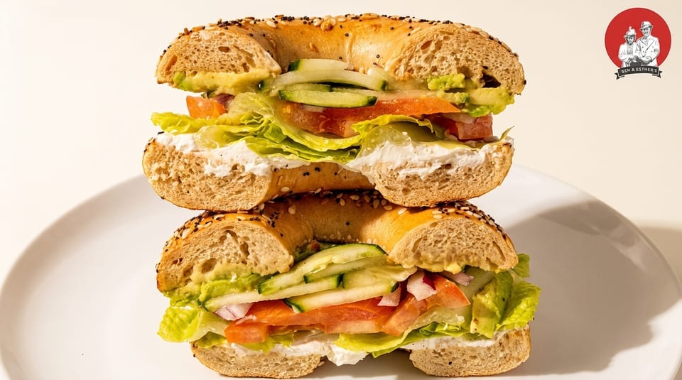 Two stacked bagels from Ben & Esther's, filled with cream cheese, lettuce, tomato, cucumber, and avocado.