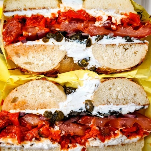 Two large bagels, sliced in half, filled with cream cheese, red peppers, and capers.