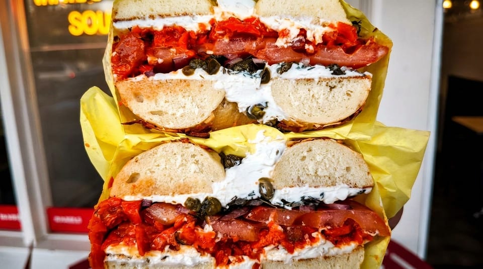 Two large bagels, sliced in half, filled with cream cheese, red peppers, and capers.