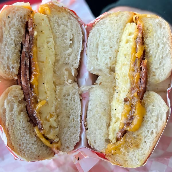 A bagel sandwich stacked with vegan bacon, egg, and melted cheese.