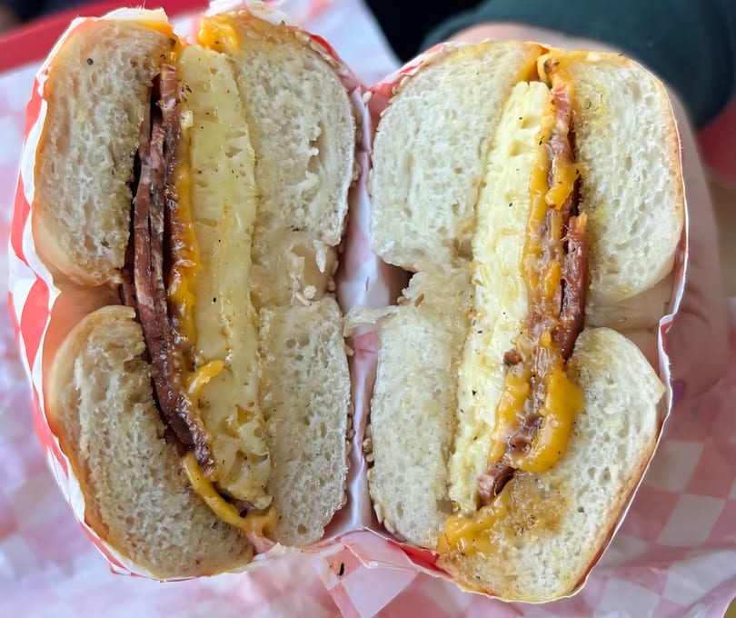 A bagel sandwich stacked with vegan bacon, egg, and melted cheese.