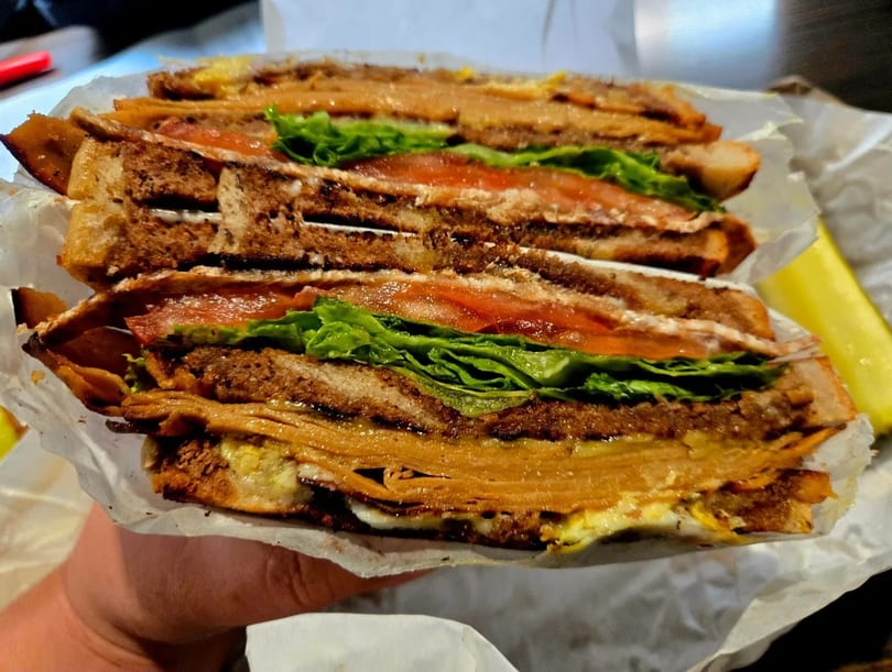 A large, layered sandwich with meat, lettuce, and tomato, held in a hand.